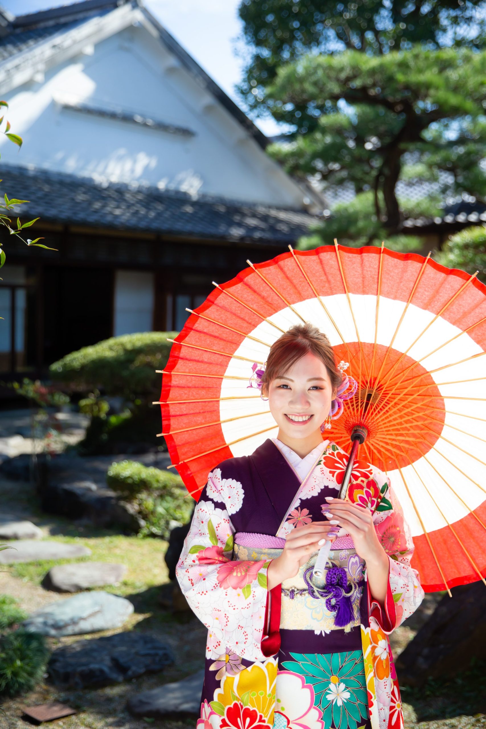 日本庭園で、笑顔で和傘をさす紫色の振袖を着た女性