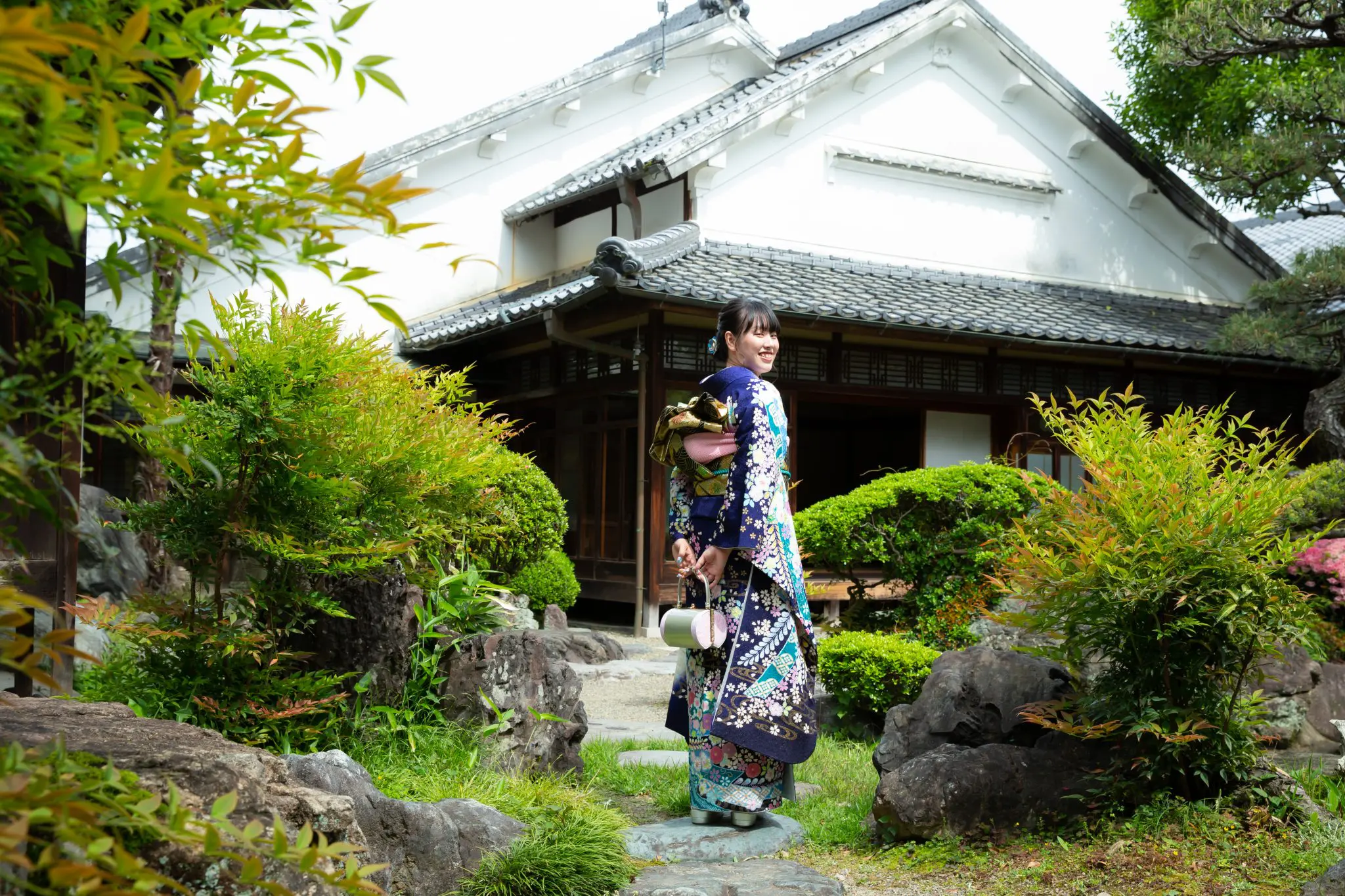 日本庭園を歩く青色の振袖を着た女性の後り姿