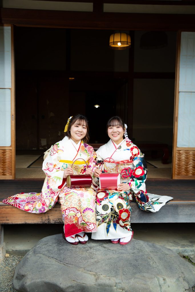 縁側に並んで座る振袖姿の姉妹