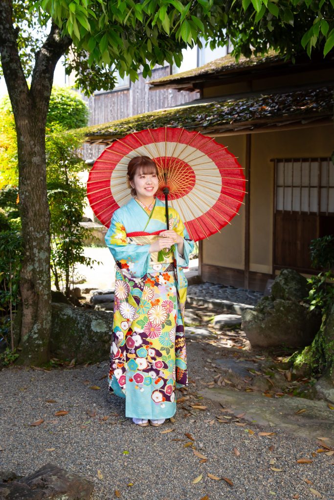 日本庭園で和傘をさしている水色の振袖を着た女性