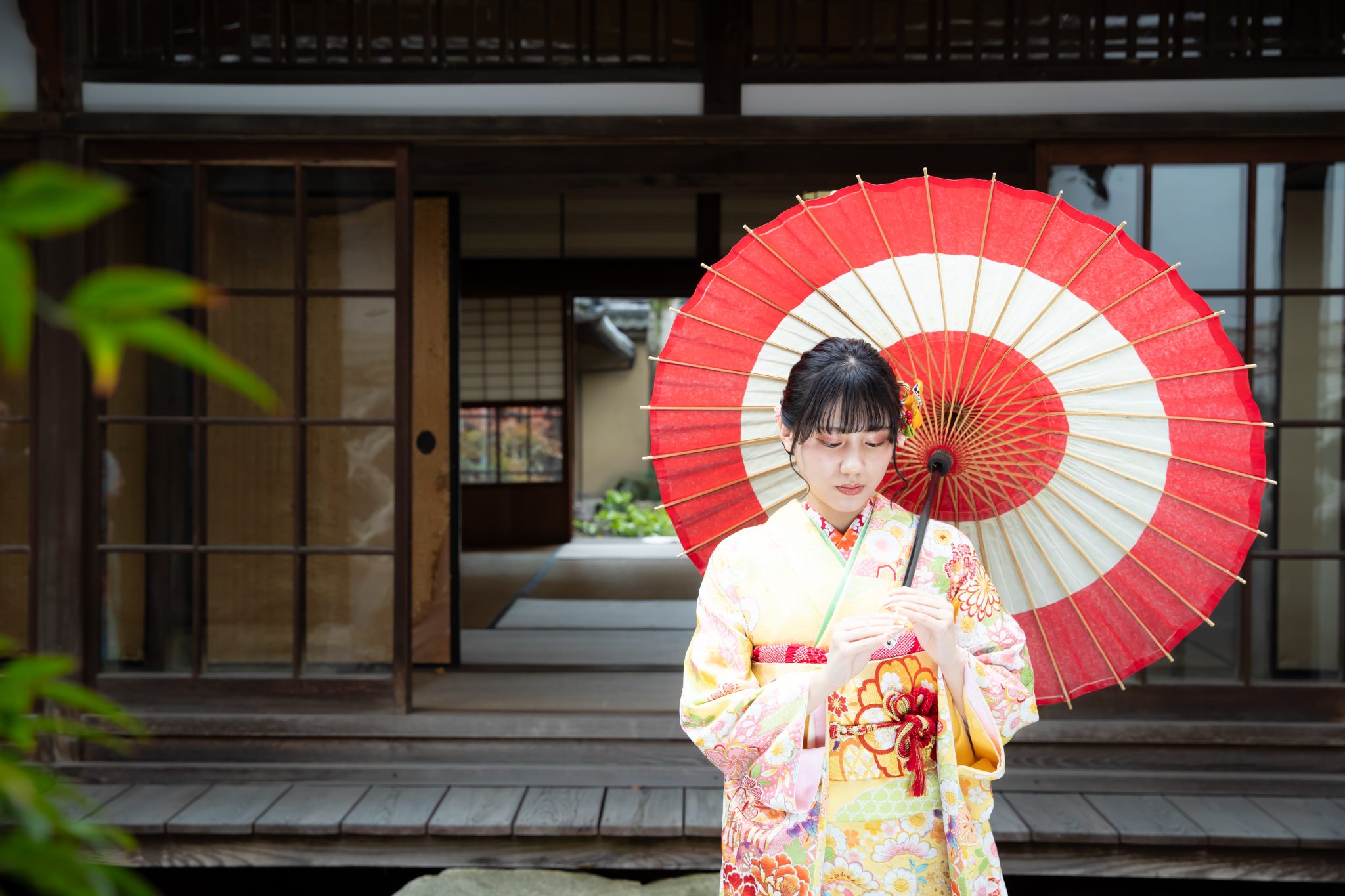 縁側の前に和傘をさして佇む黄色振袖を着た女性