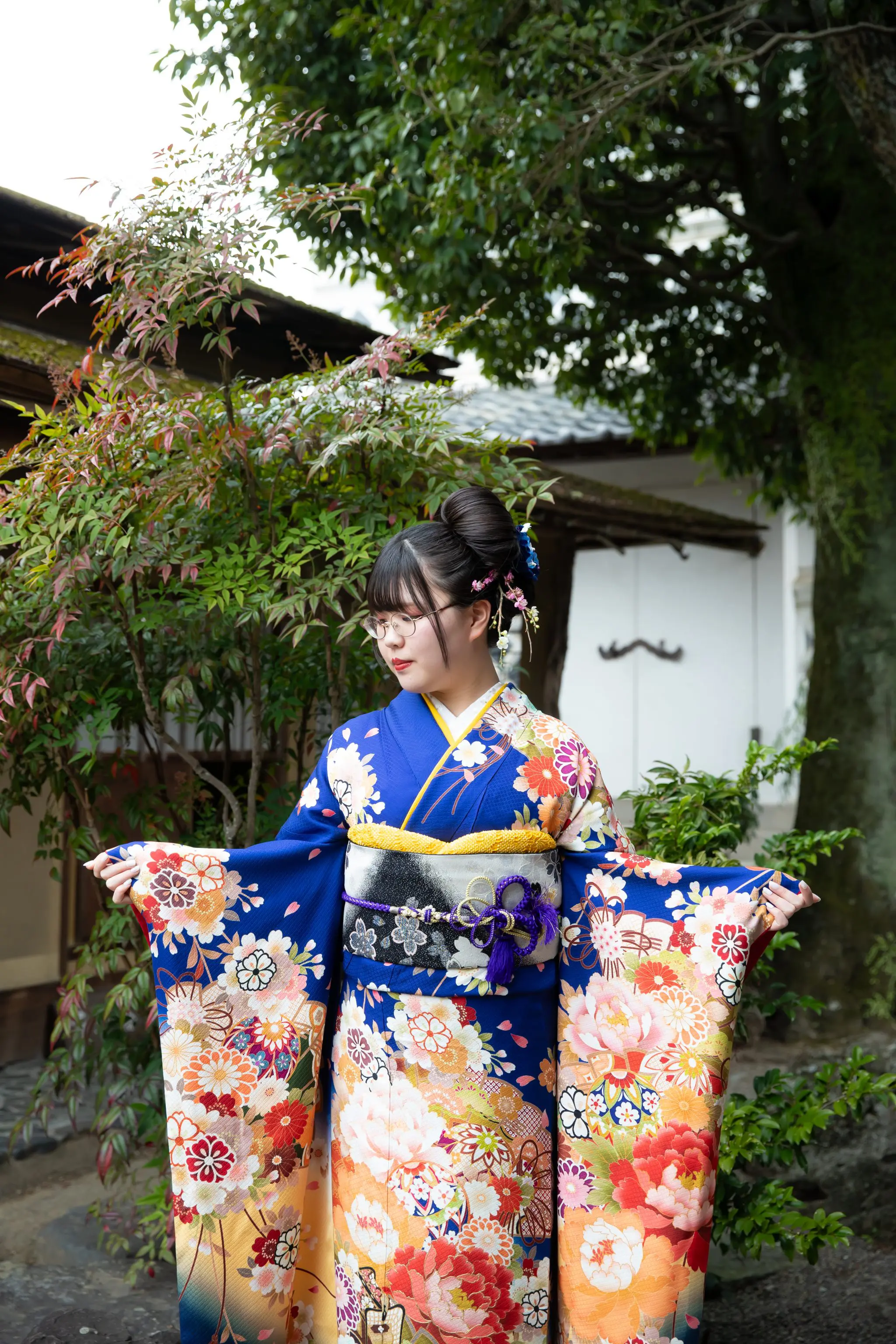 日本庭園で青い振袖の袖を広げる女性