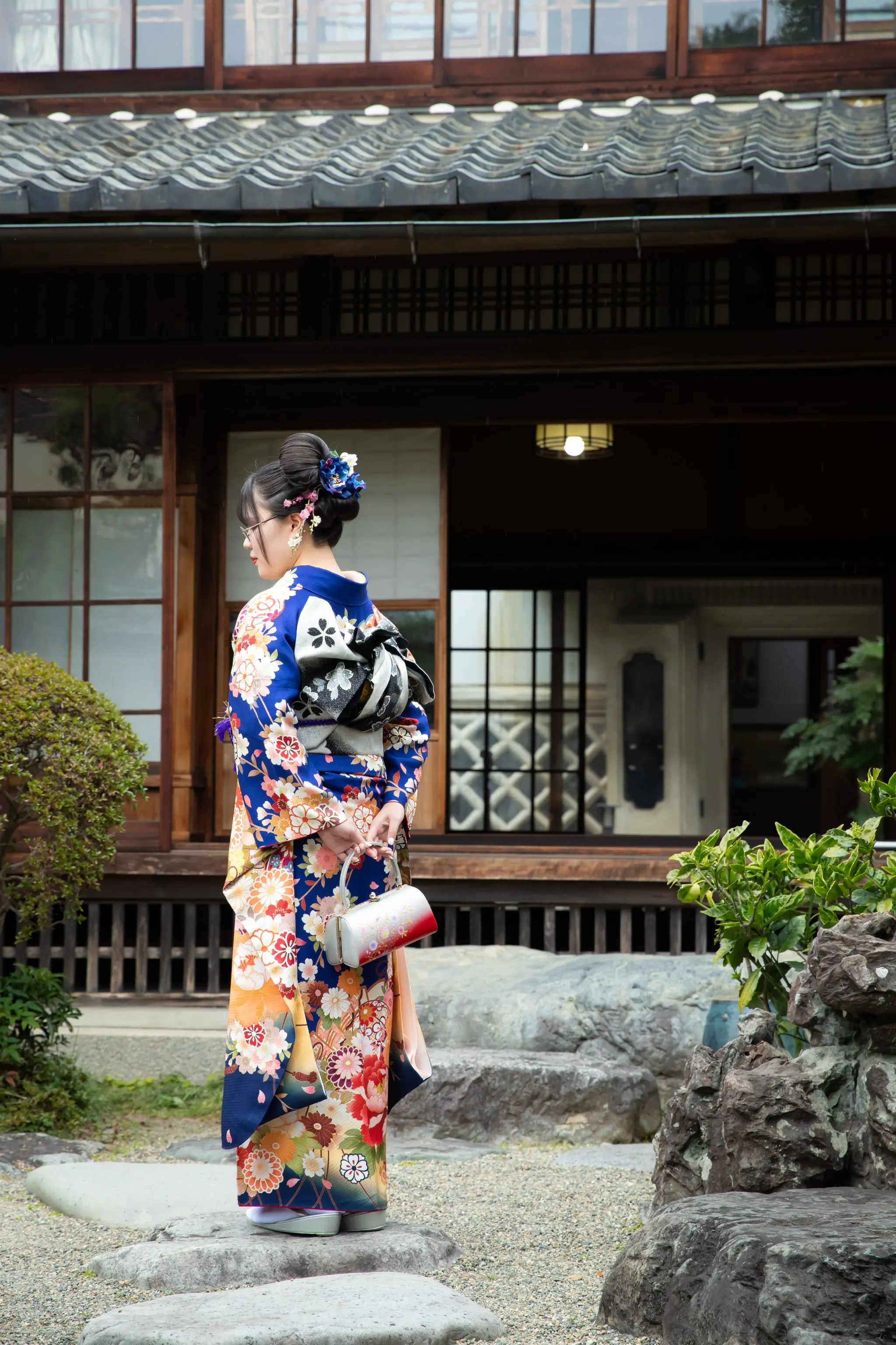 日本庭園に佇む青い振袖の女性の後ろ姿