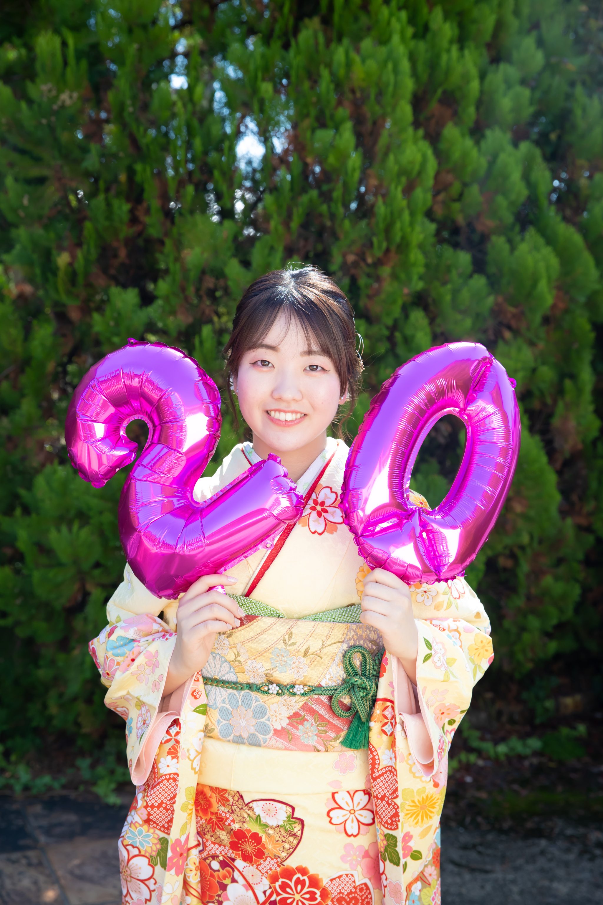 20のバルーンをもつ黄色の振袖を着た女性
