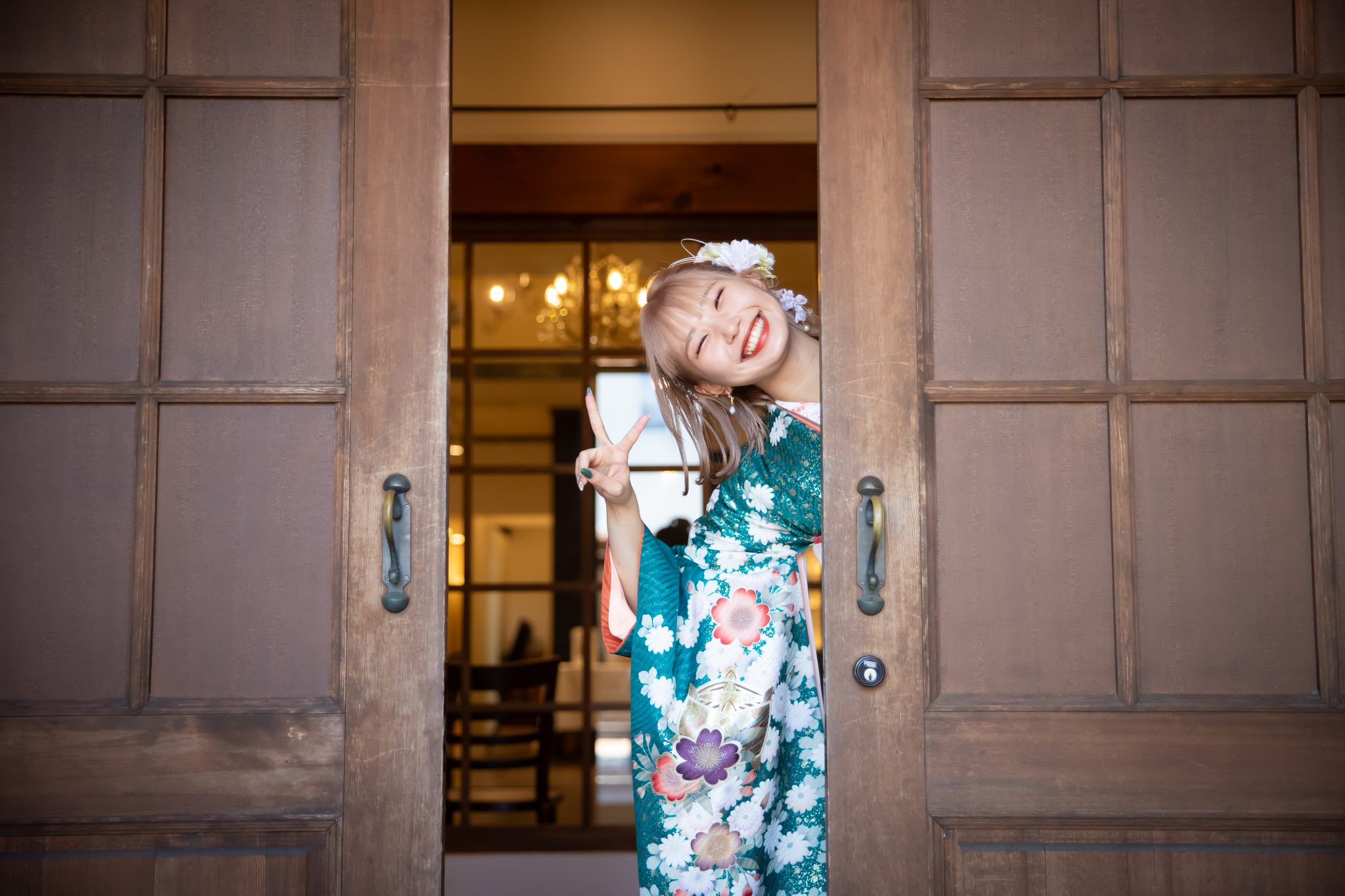開いたドアの間から顔を覗かせる青緑色の振袖を着た若い女性