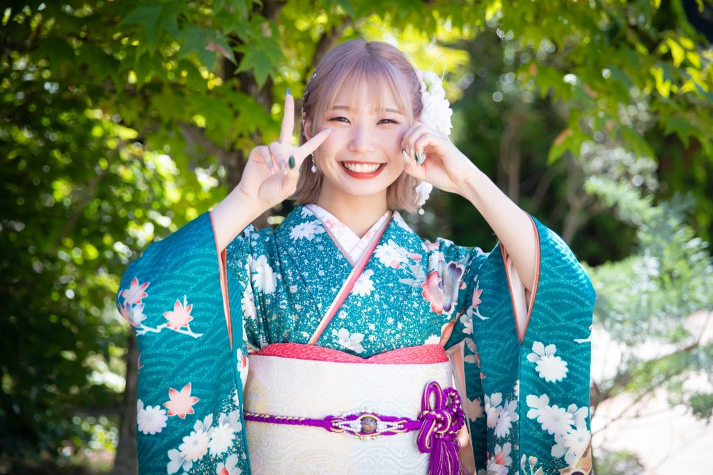 青緑色の振袖を着て笑顔で二十歳ポーズをする女性